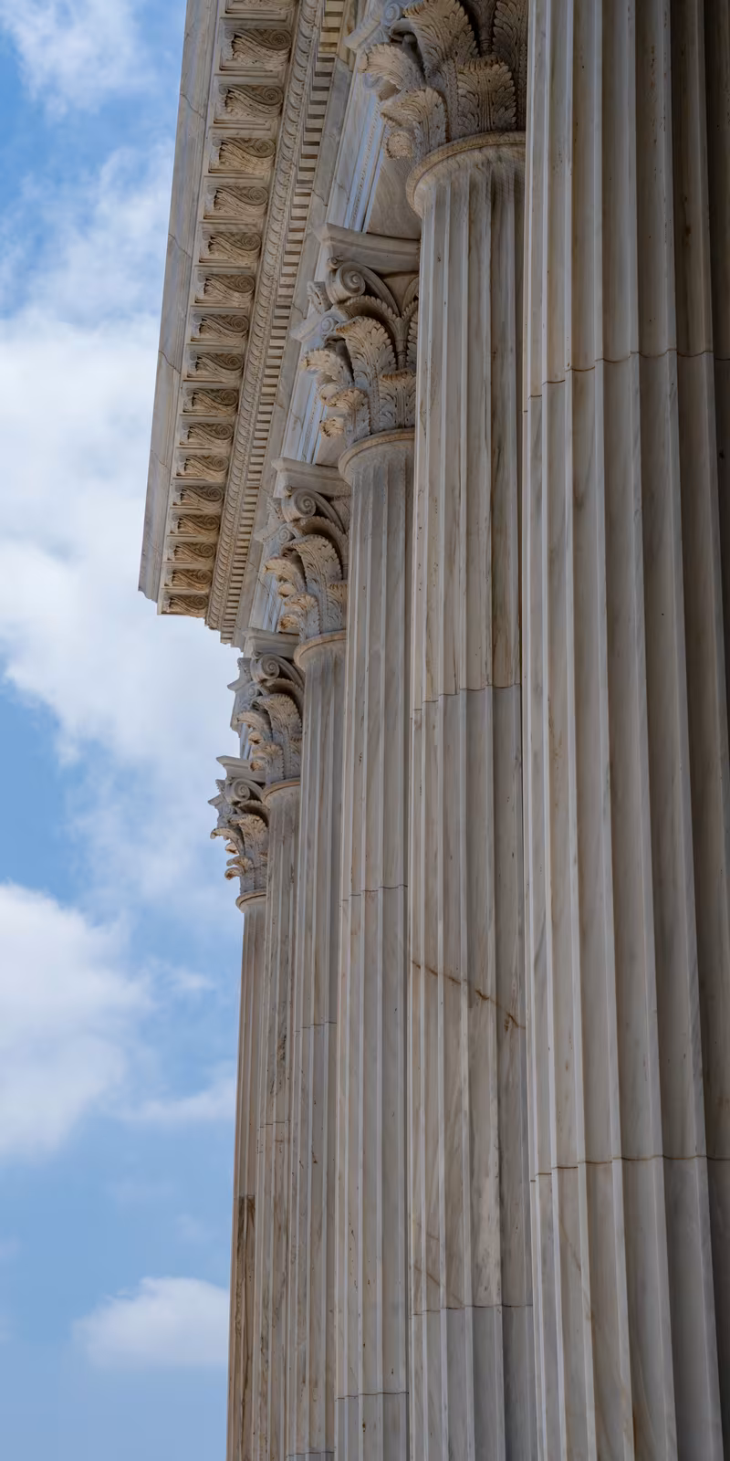 Columnas de mármol y capiteles tallados de una Casa de Adoración Bahá’í contra un cielo azul.